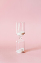 Hourglass on pink background, sand flowing through the bulb of sandglass measuring time. minimal concept.
