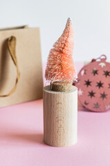 Coconut fiber orange Christmas tree on wooden stand, kraft paper gift bag on pink white background, zero waste festive concept.