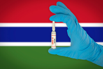 New coronavirus vaccine with the flag of Gambia in the background. Gambia medical research and vaccine development center. Doctor holding coronavirus vaccine in his hand.