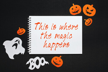 Happy halloween holiday concept. Notepad with text This is where the magic happens on black background with bats, pumpkins and ghosts