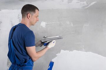 a man in blue special clothes repairs a concrete wall, side view