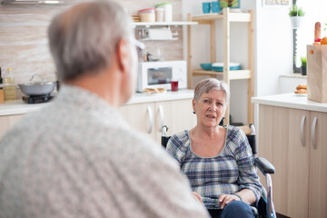 Gray Haired man chatting with paralysed wife. Retired invalid woman in wheelchair having a...