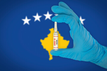New coronavirus vaccine with the flag of Kosovo in the background. Kosovo medical research and vaccine development center. Doctor holding coronavirus vaccine in his hand.