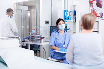 Disabled elderly man in wheelchair on hospital corridor talking with dorctor and wearing face mask...