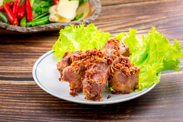 Thai deep-fried crispy pork with herb on white plate and wooden table. Food concept.