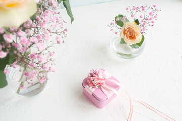 pink gift box on a white table, rose and gypsophila in a glass vase..