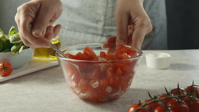 Hands of a man stirring a tomato and garlic salad with a spoon