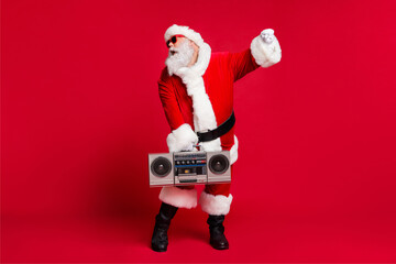 Full length photo of pensioner old man grey beard hold boom box dance hip hop wear santa x-mas costume gloves coat belt sunglass headwear black boots isolated red color background