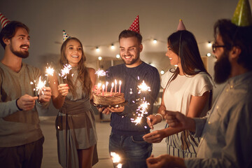 Group of happy young people with sparklers celebrating their friend's birthday at home