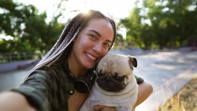 A cute beige pug puppy is trying to lick the face. A woman holds camera and squints