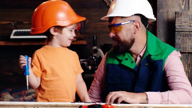 Child learning use tools with dad. Parent in protective helmet teaching little son to use different tools in school workshop. Fatherhood concept. Father and son working together.