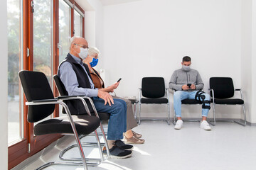 Senior couple with face masks sitting in a waiting room of a hospital together with a young man