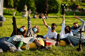 Young multi ethnic group of people watching movie at poof in open air cinema wear at mask during...