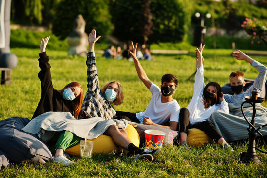 Young Multi Ethnic Group Of People Watching Movie At Poof In Open Air Cinema Wear At Mask During Covid Coronavirus Quarantine.