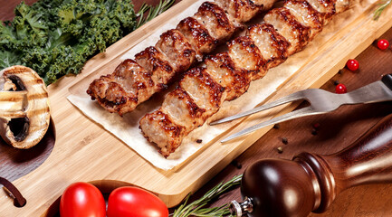 Lula kebab fried on charcoal with vegetables and spices on a wooden board.