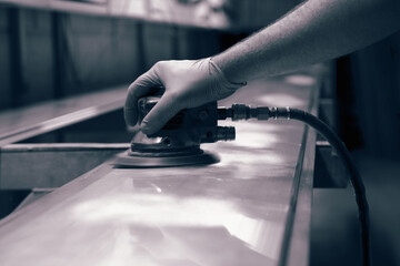 Man using orbital sander to prepare a metal panel.  With colour toning