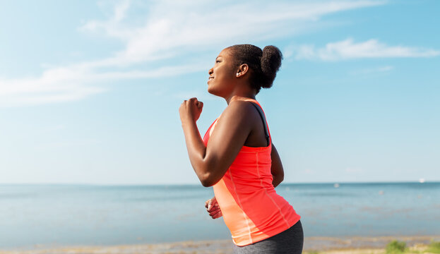 fitness, sport and healthy lifestyle concept - young african american woman running at seaside
