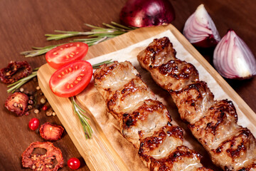 Lula kebab fried on charcoal with vegetables and spices on a wooden board.