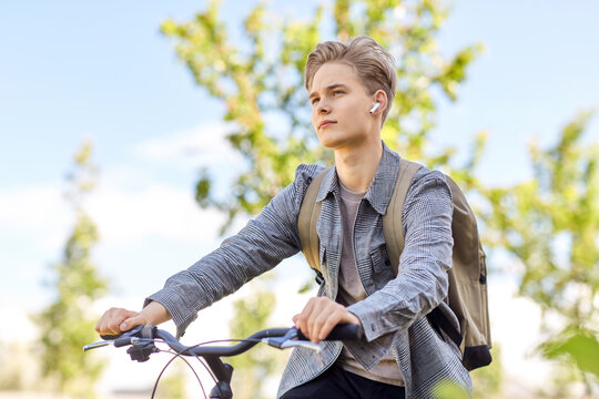 lifestyle, transport and people concept - young man or teenage student boy with backpack and earphones riding bicycle on city street