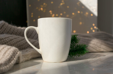 Obraz na płótnie Canvas White cup, beige warm knitted sweater, fir branches and Christmas lights on background