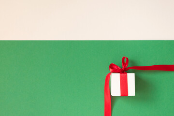 White gift box with red ribbon on green and beige background