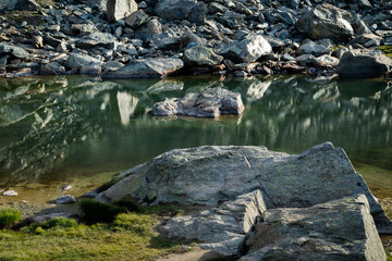 Fototapeta na wymiar Rocks reflected in the green water of a small lake in the Valais Alps of Switzerland. 