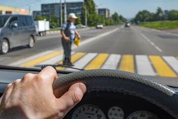 driver hand on the steering wheel of a car against the background of a pedestrian passing through a Zebra crossing