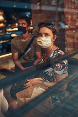Family sitting in coffee shop at store front in the city center in the evening, wearing the face mask to avoid virus infection and to prevent the spread of disease in time of coronavirus