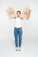 Fototapeta na wymiar young joyful woman holding shopping bags with black friday lettering on white
