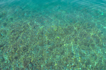 Fototapeta na wymiar Texture of transparent shallow water surface. Rippling water background. Aerial view rocky bottom of Adriatic sea in sunny day. Journey Croatia.