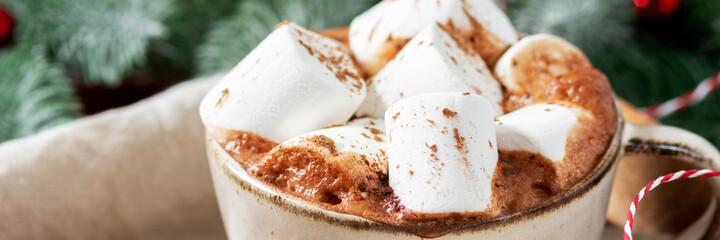Hot cocoa or hot chocolate with marshmallows in a ceramic Cup surrounded by gingerbread, Christmas tree branches and ornaments on a brown wooden table. Christmas or new year's composition