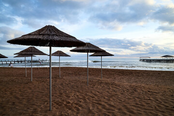 Sandy beach and umbrellas in a evening and sky with clouds in the background. Tourist beach without people at the end of the season. The resort is closed during COVID-19 pandemic