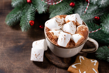 Hot cocoa or hot chocolate with marshmallows in a ceramic cup surrounded by gingerbread, Christmas tree branches and decorations on a brown wooden table. New Year or Christmas flatly