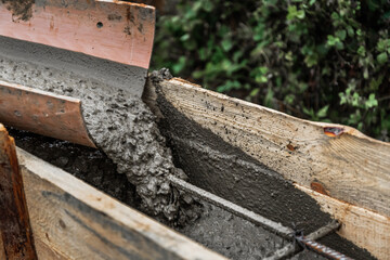 The concrete mixer unloads the concrete through a chute into a timber formwork with metal...