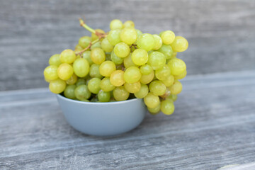 A bunch of ripe green grapes in a gray container on a gray background.