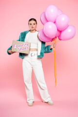 young woman holding carton box with favorite shoes lettering and balloons while standing on pink