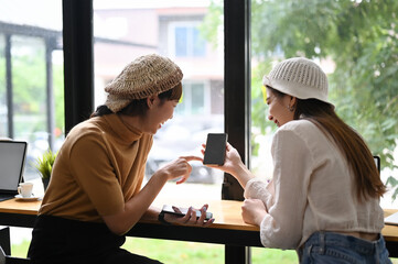 Two female freelancer sharing information on smartphone to colleague in office.