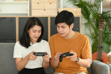 Young couple sitting on couch and using joystick to play game together.