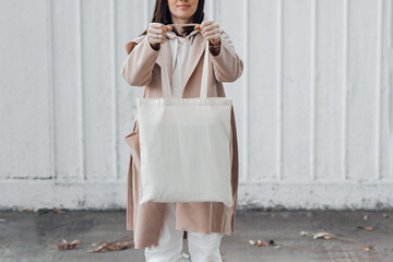 Woman in coat with white cotton bag in her hands. Mockup and zero waste concept.