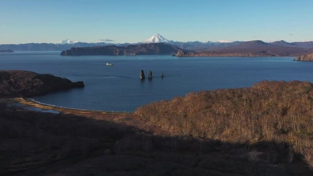 Autumn scenery, beautiful sunrise over Avacha Bay on Russia's Kamchatka Peninsula, and the famous Three Brothers Rock. The waters of the Pacific Ocean. In the background is the Avachinsky volcano.