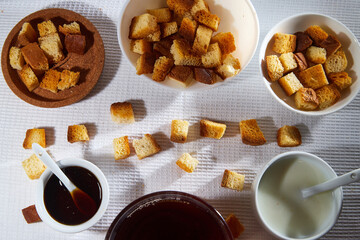 Square toasted pieces of homemade delicious rusk, hardtack, Dryasdust, zwieback, Liquid honey in a plate and cap of milk on a white tablecloth.