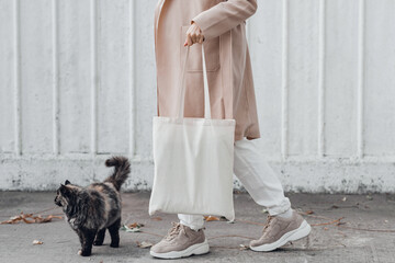 Woman in coat with white cotton bag in her hands and cute cat sitting near. Mockup and zero waste...