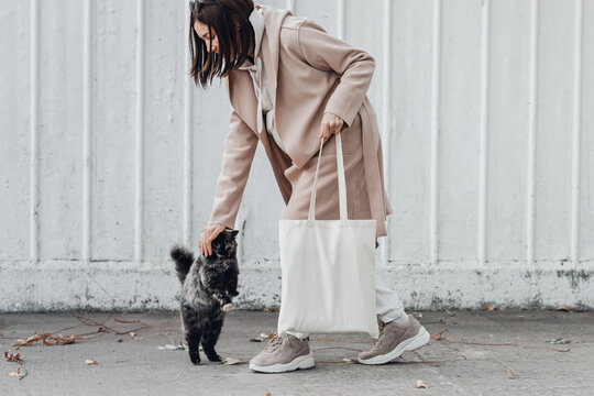 Woman in coat with white cotton bag in her hands and cute cat sitting near. Mockup and zero waste concept.