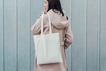 Woman in coat with white cotton bag in her hands. Mockup and zero waste concept.