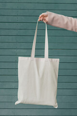 White cotton bag in woman's hand on wooden background. Mockup and zero waste concept.