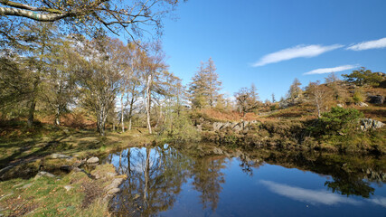 Fototapeta na wymiar Autumn colours reflected in a Lake District tarn above derelict slate quarries at Hodge Close