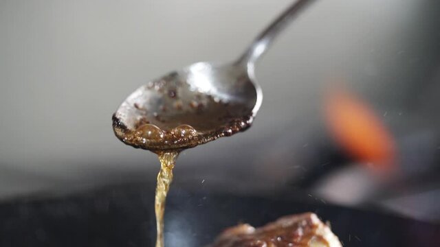 chef pouring oil with a spoon over an steack in a pan