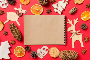 Top view of notebook, red background decorated with festive toys and Christmas symbols reindeers and New Year trees. Holiday concept
