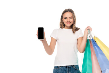 joyful young woman holding smartphone with blank screen near colorful shopping bags isolated on white