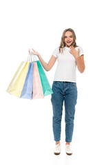 excited young woman holding colorful shopping bags and looking at camera isolated on white
